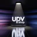Logo UPV shop bianco posizionato al centro di un palcoscenico scuro, illuminato da un riflettore dall'alto con riflesso nitido sul pavimento lucido e sfondo con scie luminose blu e viola.